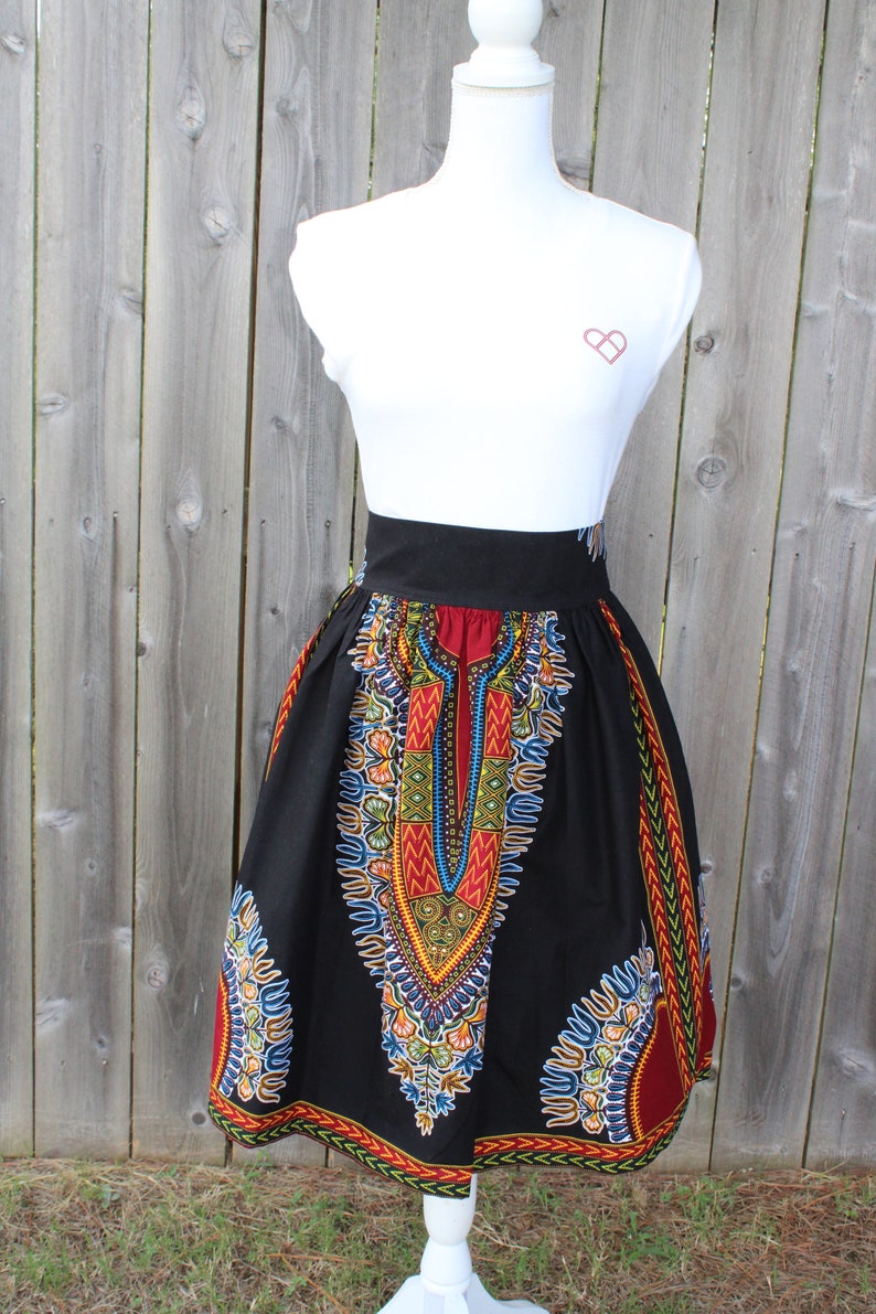 May include: A black knee-length skirt with a vibrant, colorful pattern. The skirt features a high waist and a bold, geometric design in red, yellow, blue, and green. The skirt is displayed on a white mannequin.