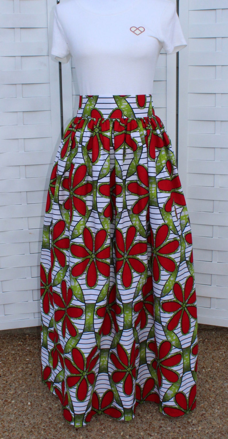 Peut inclure: Un t-shirt blanc avec un petit motif de c&oelig;ur marron et une longue jupe taille haute. La jupe pr&eacute;sente un motif floral vibrant avec des fleurs rouges, des feuilles vertes et des rayures blanches et noires.