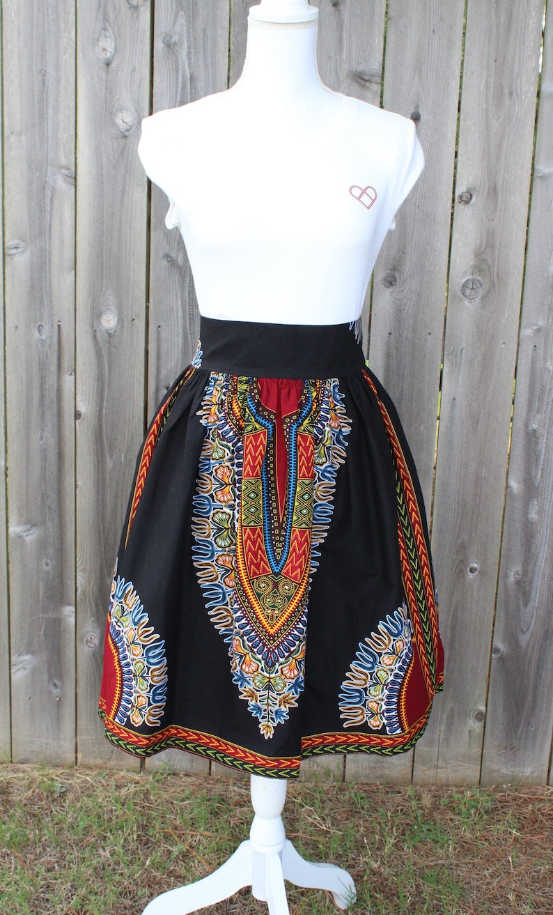 May include: A black skirt with a vibrant, colorful African print design. The skirt features a high waist and a knee-length hemline. The print includes red, yellow, blue, and green patterns. The skirt is displayed on a white mannequin.