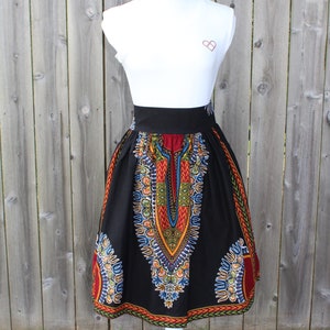 May include: A black skirt with a vibrant, colorful African print. The skirt features a wide black waistband and a flared silhouette. The print includes red, yellow, blue, and green geometric patterns. The skirt is displayed on a white mannequin.
