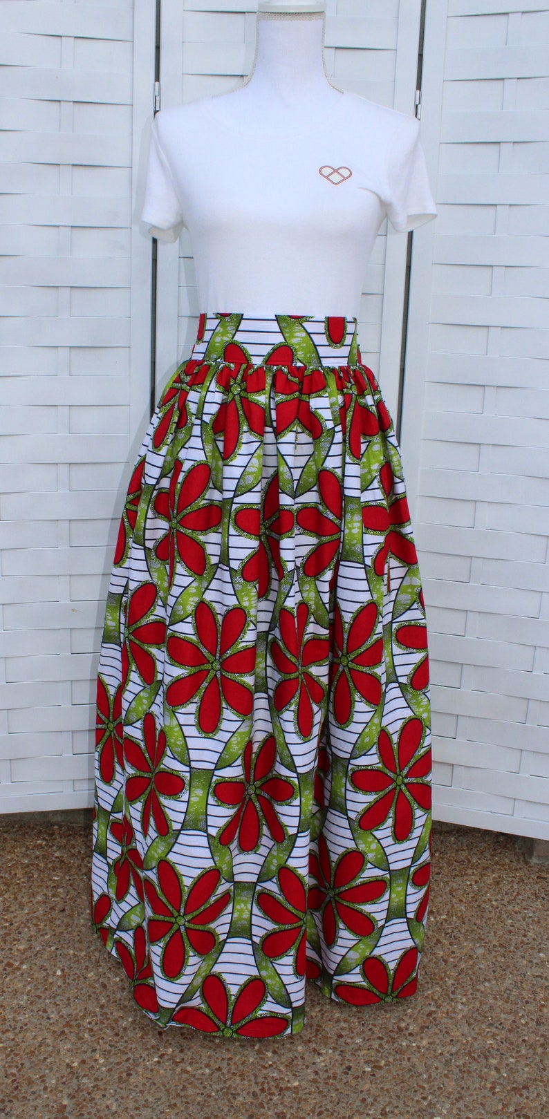Peut inclure: Un t-shirt blanc avec un petit motif de double c&oelig;ur est associ&eacute; &agrave; une longue jupe fluide. La jupe pr&eacute;sente un motif floral vibrant en rouge et vert sur fond blanc avec des rayures noires. La jupe est fronc&eacute;e &agrave; la taille.