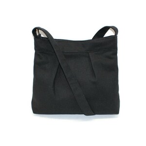 May include: A black crossbody bag with a long, adjustable strap. The bag is made of a solid, matte fabric and features a pleated design on the front. The bag has a rectangular shape and a simple, minimalist style.