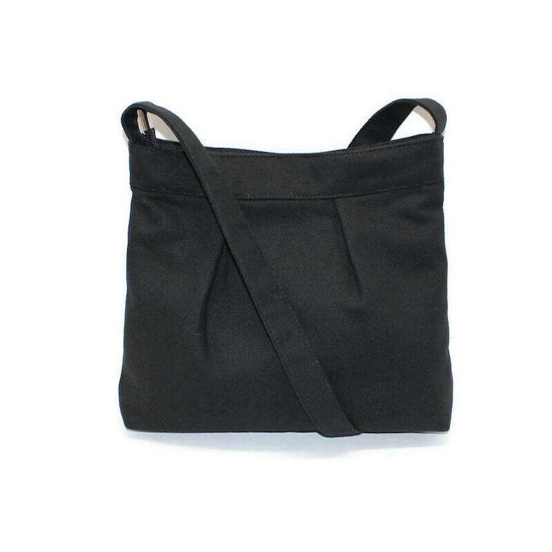 May include: A black crossbody bag with a long, adjustable strap. The bag is made of a solid, matte fabric and features a pleated design on the front. The bag has a rectangular shape and a simple, minimalist style.