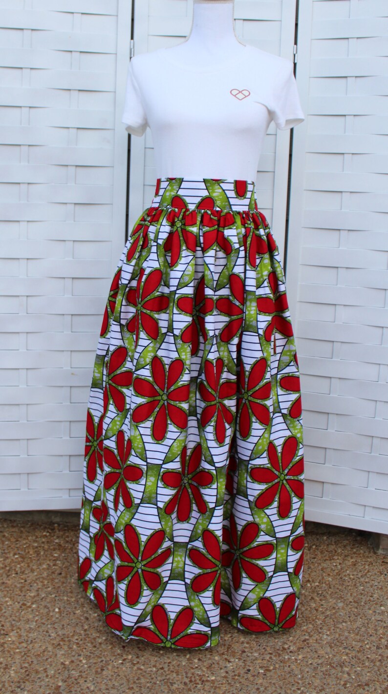Peut inclure: Longue jupe ample avec un motif floral vibrant. La jupe pr&eacute;sente de grandes fleurs rouges avec des accents verts sur un fond blanc avec des rayures noires. Elle est associ&eacute;e &agrave; un t-shirt blanc.