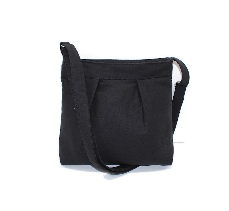 May include: A black crossbody bag with a rectangular shape and a long, adjustable strap. The bag features a pleated design on the front and a simple, minimalist aesthetic. The strap is attached to the bag with metal hardware.