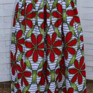 Peut inclure: Longue jupe pliss&eacute;e avec un motif floral vibrant. Le motif pr&eacute;sente de grandes fleurs rouges avec des feuilles vertes sur un fond blanc avec des rayures noires. La jupe est en tissu l&eacute;ger.