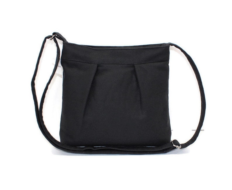 May include: A black crossbody bag with a long, adjustable strap. The bag is made of a solid, dark fabric with a simple, pleated design on the front. The strap is attached with silver-colored metal rings.