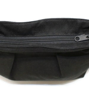 May include: A black fanny pack with a zippered closure. The bag has a rectangular shape with a curved top and a black adjustable strap. The zipper is black and the hardware is silver.
