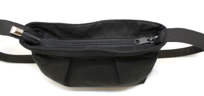 May include: A black fanny pack with a zippered closure. The bag has a rectangular shape with a curved top and a black adjustable strap. The zipper is black and the hardware is silver.