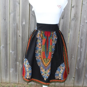 May include: A black skirt with a vibrant, colorful African print design. The skirt features a high waist and a flared silhouette. The print includes red, yellow, blue, and green patterns. The skirt is displayed on a white mannequin.