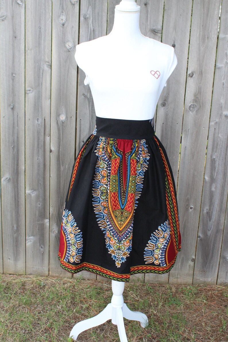 May include: A black skirt with a vibrant, colorful African print design. The skirt features a high waist and a flared silhouette. The print includes red, yellow, blue, and green patterns. The skirt is displayed on a white mannequin.