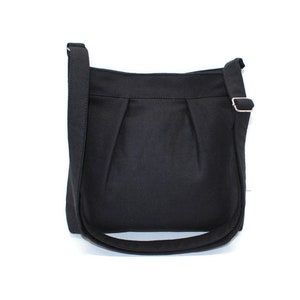 May include: A black crossbody bag with a long, adjustable strap and a silver-colored buckle. The bag has a simple, pleated design on the front and a curved bottom. The bag is made of a solid, dark fabric.
