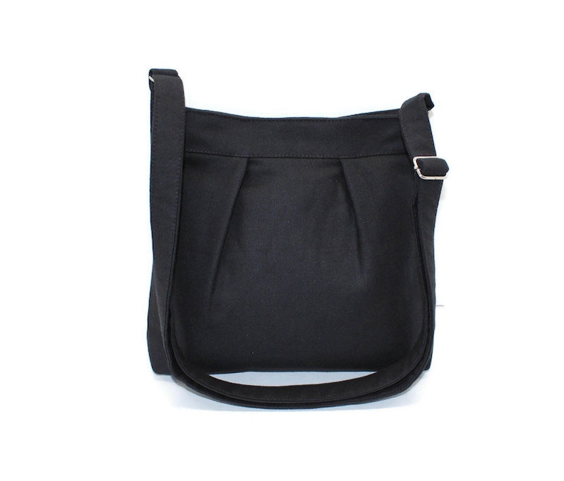 May include: A black crossbody bag with a long, adjustable strap and a silver-colored buckle. The bag has a simple, pleated design on the front and a curved bottom. The bag is made of a solid, dark fabric.