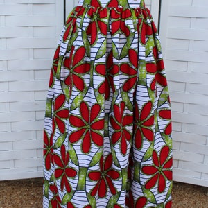 Peut inclure: Un t-shirt blanc avec un petit motif de c&oelig;ur associ&eacute; &agrave; une longue jupe pliss&eacute;e. La jupe pr&eacute;sente un motif floral vibrant en rouge et vert sur fond blanc avec des rayures noires. La jupe est de style long.