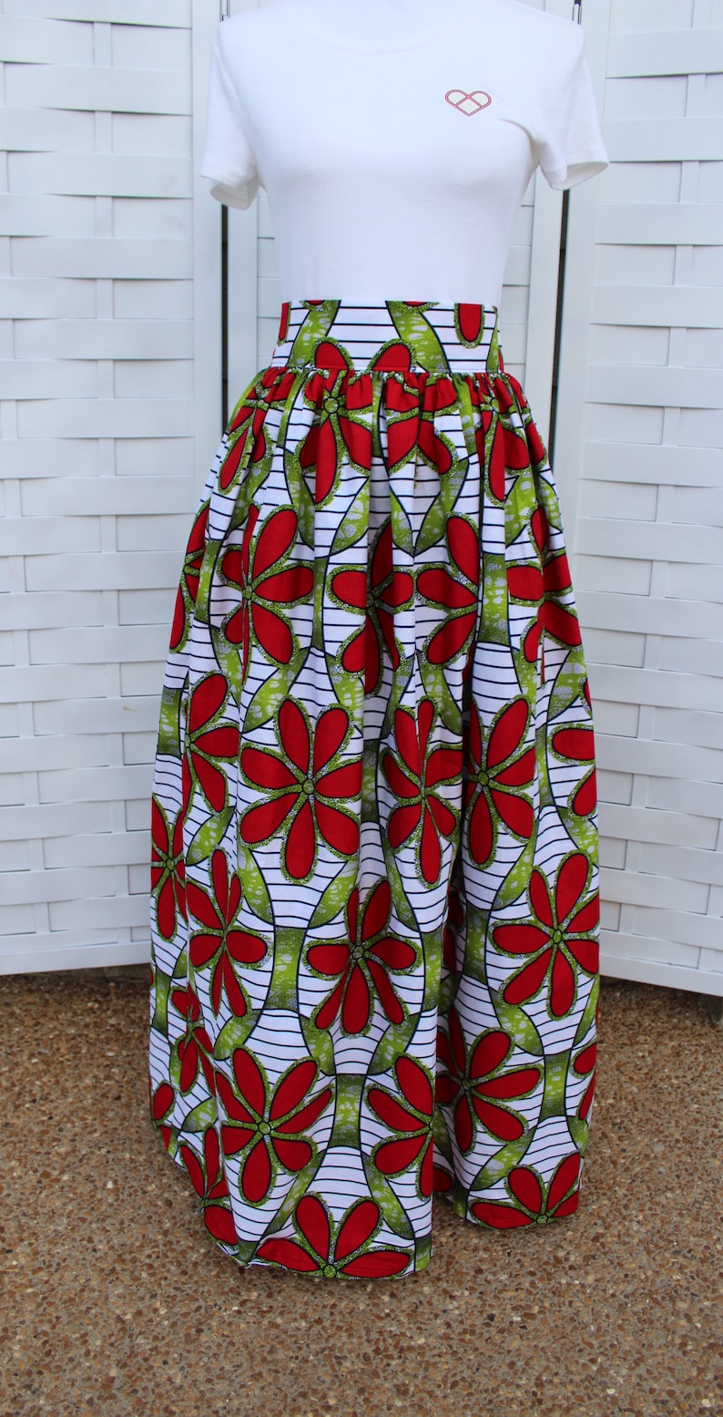 Peut inclure: Un t-shirt blanc avec un petit motif de c&oelig;ur associ&eacute; &agrave; une longue jupe pliss&eacute;e. La jupe pr&eacute;sente un motif floral vibrant en rouge et vert sur fond blanc avec des rayures noires. La jupe est de style long.