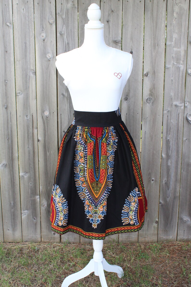 May include: A black skirt with a vibrant, colorful pattern. The skirt features a wide black waistband and a knee-length hem. The design includes red, yellow, blue, and green accents, creating a bold and eye-catching look.
