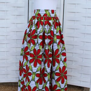 Peut inclure: Un t-shirt blanc avec un petit motif de c&oelig;ur, associ&eacute; &agrave; une longue jupe. La jupe pr&eacute;sente un motif floral vibrant en rouge et vert sur fond blanc. Le design de la jupe est audacieux et accrocheur.