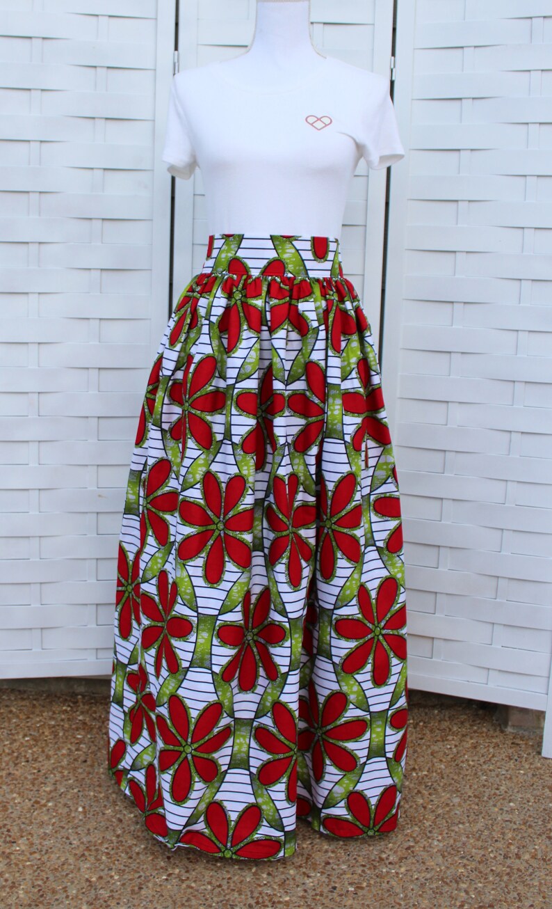 Peut inclure: Un t-shirt blanc avec un petit motif de c&oelig;ur, associ&eacute; &agrave; une longue jupe. La jupe pr&eacute;sente un motif floral vibrant en rouge et vert sur fond blanc. Le design de la jupe est audacieux et accrocheur.