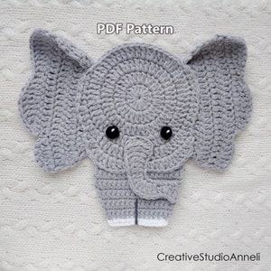 May include: A grey crocheted elephant head with black eyes and a white crocheted trunk. The elephant is on a white crocheted background. The text "PDF Pattern" is at the top of the image. The text "CreativeStudioAnnelli" is at the bottom of the image.