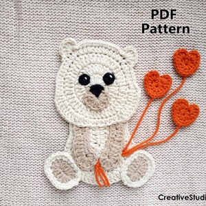 May include: Crochet pattern for a white bear holding orange heart balloons. The pattern is available as a PDF download. The text "PDF Pattern" is visible in the image. The text "CreativeStudioAnneli" is visible in the image.