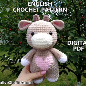 May include: Crochet pattern for a plush brown and pink cow toy with a white face. The pattern is available as a digital PDF download. The text "ENGLISH CROCHET PATTERN" and "DIGITAL PDF" is visible in the image.