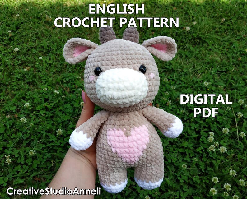 May include: Crochet pattern for a plush toy cow with a pink heart on its chest. The cow is gray with white accents and black eyes. The pattern is available as a digital PDF download. The text "ENGLISH CROCHET PATTERN" and "DIGITAL PDF" is visible in the image.