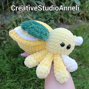 Può includere: Un polpo all'uncinetto giallo fatto a mano con un design a fetta di limone. Il polpo ha occhi di sicurezza neri, dettagli bianchi e una foglia verde. Il testo "CreativeStudioAnneli" è nella parte superiore dell'immagine.