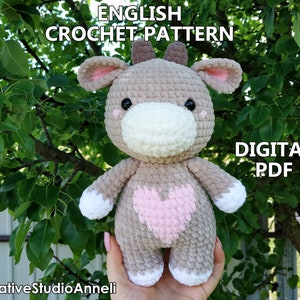 May include: Crochet pattern for a plush brown and white cow with a pink heart on its chest. The pattern is available as a digital PDF download. The text "ENGLISH CROCHET PATTERN" and "DIGITAL PDF" is visible in the image.