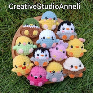May include: A selection of crocheted bird toys, including penguins and chicks, in a variety of colours, such as yellow, pink, blue, and green, arranged on a wooden tray. The toys have black and white details. The text "CreativeStudioAnneli" is at the top.