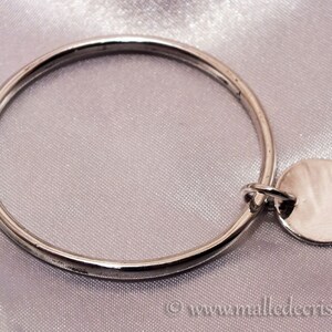 May include: A silver bangle bracelet with a round silver charm attached. The charm is smooth and has a shiny finish.