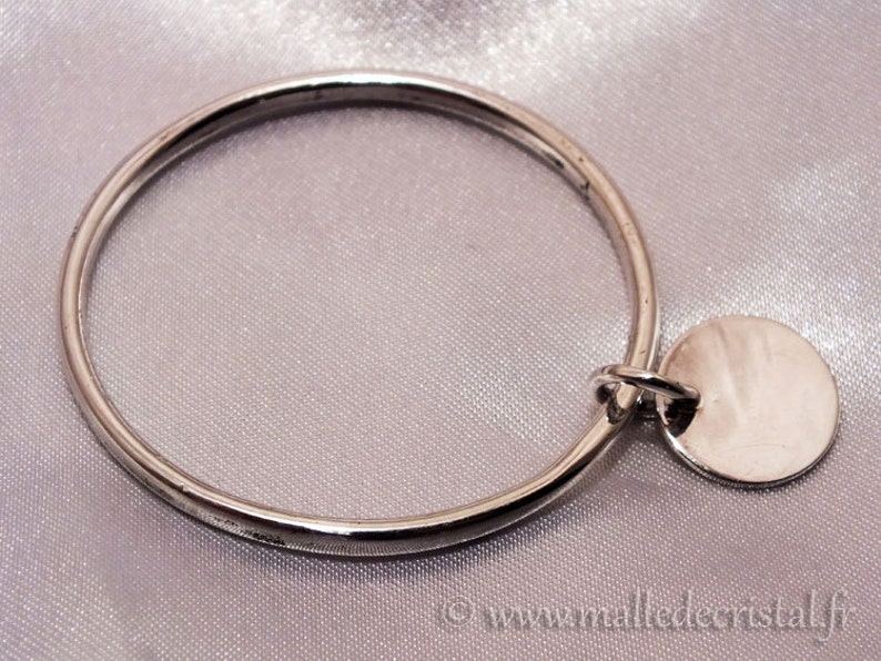 May include: A silver bangle bracelet with a round silver charm attached. The charm is smooth and has a shiny finish.