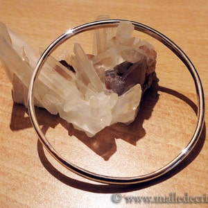 May include: A silver bangle bracelet resting on a cluster of clear quartz crystals.