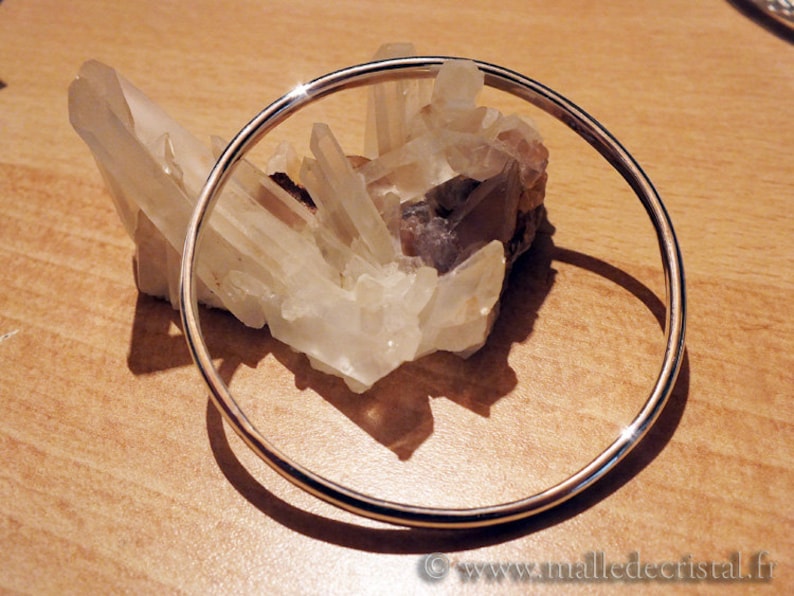 May include: A silver bangle bracelet resting on a cluster of clear quartz crystals.