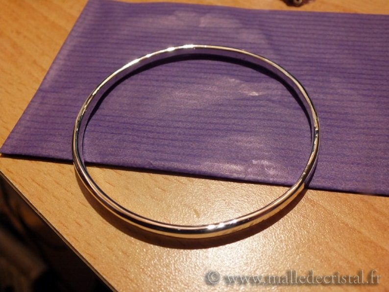 May include: A silver bangle bracelet with a hammered finish. The bracelet is lying on a purple surface.