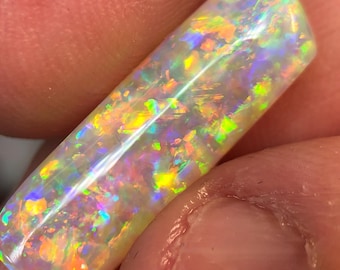 May include: A white opal gemstone with a rainbow of colors, including red, orange, yellow, green, blue, and purple. The opal is cut into a long, rectangular shape.