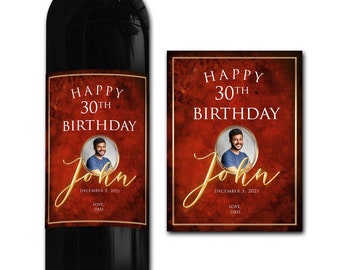 Puede incluir: Una etiqueta de botella de vino tinto con un borde dorado y una foto de una persona. La etiqueta dice "Feliz 30 cumpleaños John" con la fecha "3 de diciembre de 2021" y "Amor, Papá".