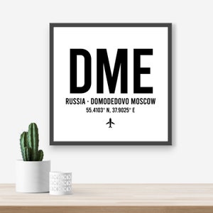 May include: Black and white airport code sign with the letters DME, the words "Russia - Domodedovo Moscow" and the coordinates "55.4103° N, 37.9025° E". A small airplane icon is below the coordinates.