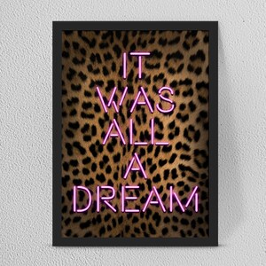 Puede incluir: Una impresión artística enmarcada con la frase "IT WAS ALL A DREAM" en letras de neón rosa brillante. El fondo es un estampado de leopardo en tonos marrones y negros. El marco es negro.