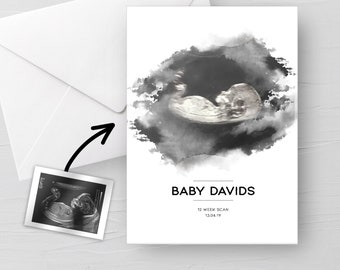 Puede incluir: Una imagen de ultrasonido en blanco y negro de un bebé en un marco de estilo acuarela. El texto "BABY DAVIDS 12 WEEK SCAN 13.04.19" está debajo de la imagen.