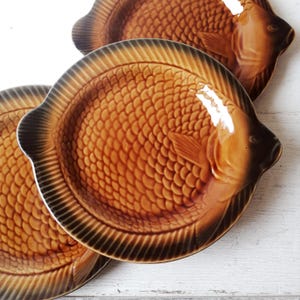 Peut inclure: Trois assiettes en céramique de forme de poisson brun avec une surface texturée. Les assiettes sont empilées les unes sur les autres.