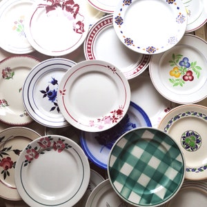 Könnte beinhalten: Eine Sammlung von Vintage-Keramiktellern mit verschiedenen floralen und geometrischen Mustern in Blautönen, Rot, Grün und Weiß. Die Teller sind kreisförmig angeordnet und bilden ein optisch ansprechendes Ensemble.