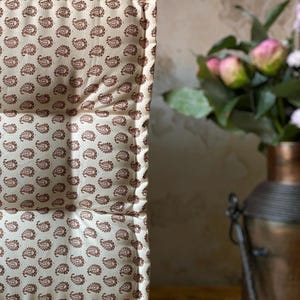 Op de afbeelding: Crèmekleurig kussen met een herhalend paisley patroon in bruintinten. Het kussen heeft een gewatteerd ontwerp en een gewatteerde uitstraling. De randen zijn netjes afgewerkt. De algehele esthetiek is vintage of bohemien. Afmetingen: ongeveer 40 cm x 40 cm.
