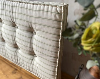 Könnte beinhalten: Ein getuftetes Kopfteil mit einem gestreiften Muster in Creme und Hellgrün. Das Kopfteil hat eine seilartige Zierleiste und ist mit Knöpfen versehen. Das Design ist im klassischen Landhausstil gehalten. Das Kopfteil steht auf einer Holzoberfläche.