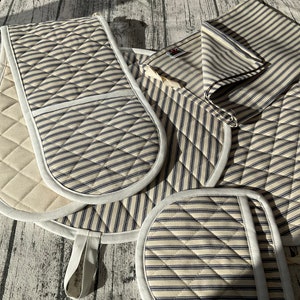 May include: Set of four blue and white striped kitchen pot holders. Two are oven mitts with a white quilted back and a white trim. Two are smaller pot holders with a white trim.