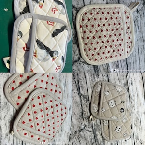 May include: A selection of quilted pot holders with different patterns. Designs include puffins, red hearts on white, and sheep. Each pot holder has a quilted design and a loop for hanging. The pot holders are made of fabric.