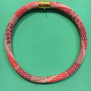 Könnte beinhalten: Eine rosafarbene und silberne Perlenkette mit einem goldenen Verschluss. Die Kette besteht aus kleinen Perlen, die in einem geometrischen Muster miteinander verwoben sind.