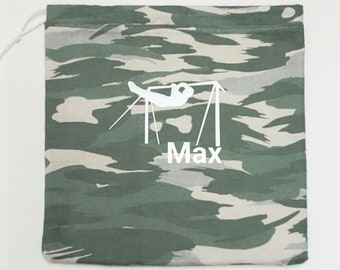 May include: A camouflage-patterned drawstring bag with a white illustration of a gymnast on a bar and the name "Max" in white. The bag features a green, grey, and beige camouflage design.