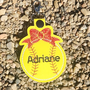 Puede incluir: Llavero de softball amarillo con un lazo rojo y el nombre Adriane bordado.