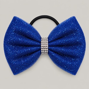 May include: A bright blue hair tie featuring a large, glittery tulle bow. The center of the bow is cinched with a band of small, clear, sparkling rhinestones. The elastic hair band attached to the back of the bow is solid black in color.