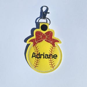 Puede incluir: Llavero de softball amarillo con un lazo rojo y el nombre Adriane bordado.
